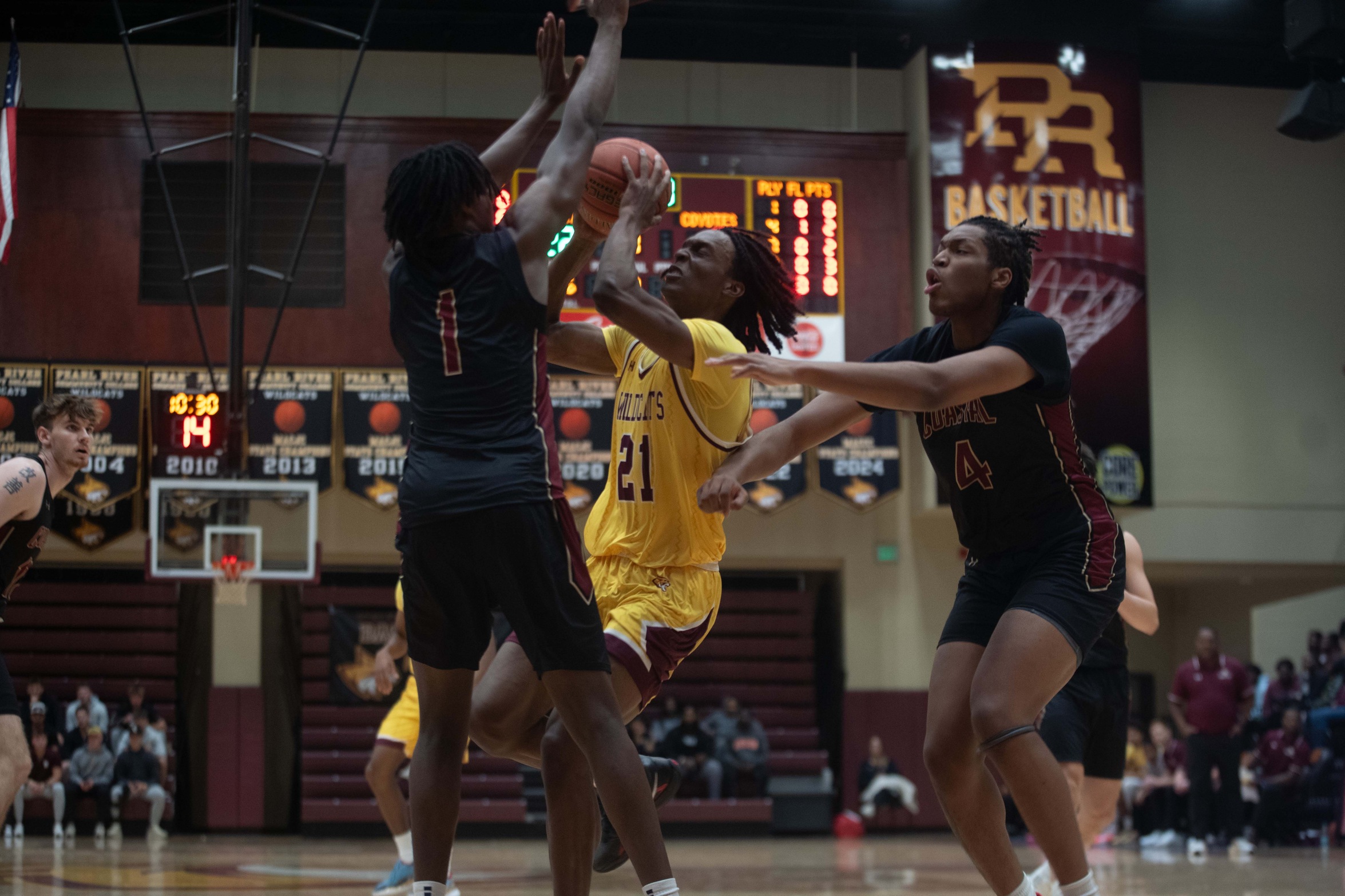 Basketball player pulls down a rebound between two defenders.